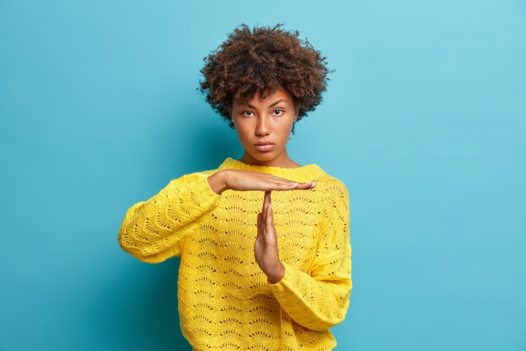 Woman in yellow sweater on blue background giving the "time out" hand signal.