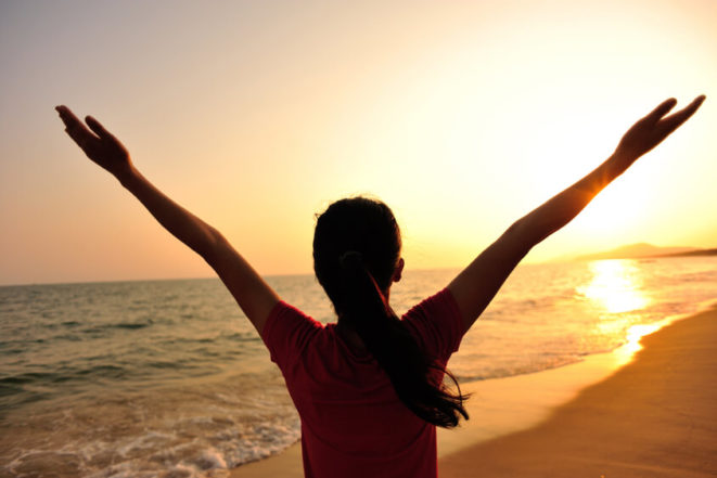 Therapies ACT cheering woman open arms at sunset seaside beach